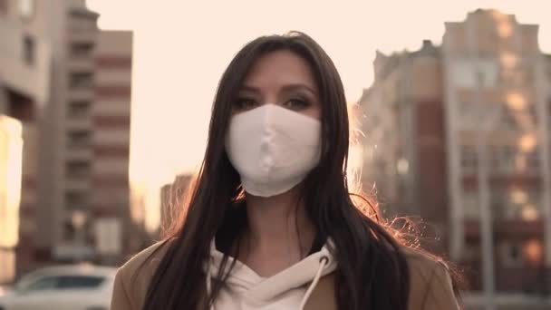 Meisje in beige jas in wit viraal masker staat in de wind — Stockvideo