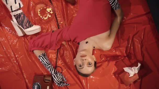 Красива дівчина в червоній сукні і стильні рукавички лежать на червоній підлозі навколо таблеток за призначенням психолога — стокове відео