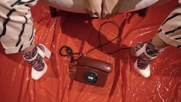 Régi telefon áll egy piros lakkozott padlón lábai között egy lány sarkú — Stock videók