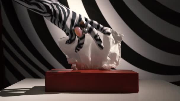 Жіноча рука в рукавичці зебри з кільцями на пальцях бере серветку з упаковки і викидає її — стокове відео