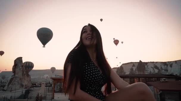 Piękna brunetka z europejskim wyglądem siedzi na tarasie w tle balonu o zachodzie słońca w Kapadocji — Wideo stockowe