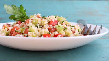 Mavi bir arka plan üzerinde beyaz bir tabak salatalık, domates ve yeşillik ile Tabula salatası