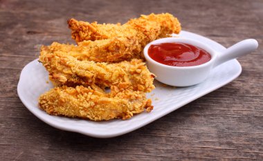 Lezzetli kızarmış tavuk göğsü şeritleri beyaz tabakta, eski ahşap masa üzerinde domates soslu 