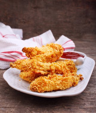 Lezzetli kızarmış tavuk göğsü şeritleri beyaz tabakta, eski ahşap masa üzerinde domates soslu 