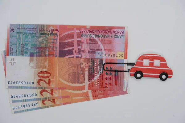 Paper clip with the image of a toy car and Swiss banknotes, saving up money for a car, credit, car loan