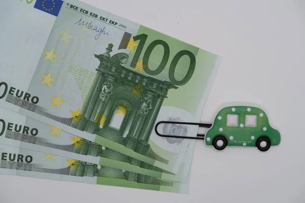 Paper clip with the image of a toy car and one hundred euro banknote, saving up money for a car, loan, car loan