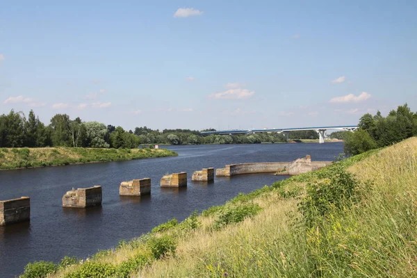 Massive concrete piers of the former pier, water surface of the river, a new bridge in the background