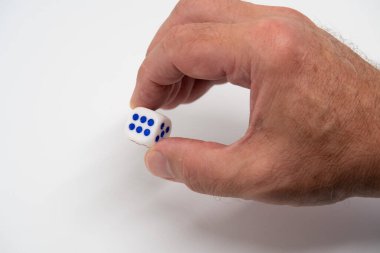 Bir adamın eli iki parmağıyla zar tutar. Tahmin edilemezliği ve belirsizliği simgeleyen bir zar.
