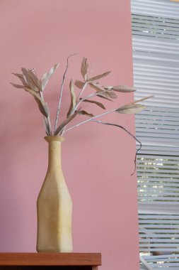 Bir duvarın arka planında yapay buket ve perdeli bir pencere.