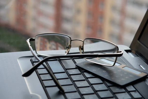 Glasses and calculator on laptop keyboard on the background of residential buildings, freelancer