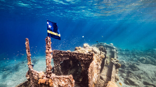 Ship wreck "Tugboat" in  shallow water of coral reef in Caribbean sea with  Curacao Flag, view to surface and sunbeams