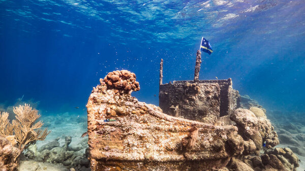 Ship wreck "Tugboat" in  shallow water of coral reef in Caribbean sea with  Curacao Flag, view to surface and sunbeams
