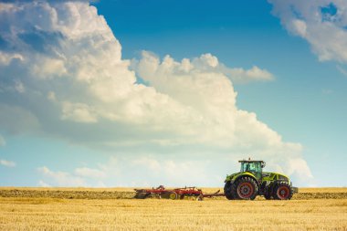 Yaz aylarında traktörün ısı alan hasat parlak güneşli gökyüzü bulutlu sonra pulluklar.
