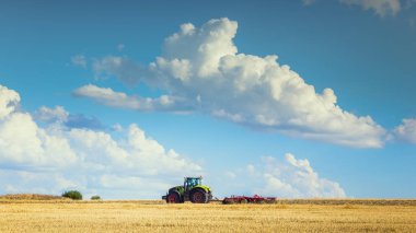 Yaz aylarında traktörün ısı alan hasat parlak güneşli gökyüzü bulutlu sonra pulluklar.