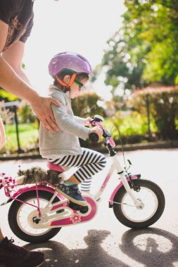 Babası küçük yürümeye başlayan çocuk kızı parkta Bisiklete binmeyi öğretir