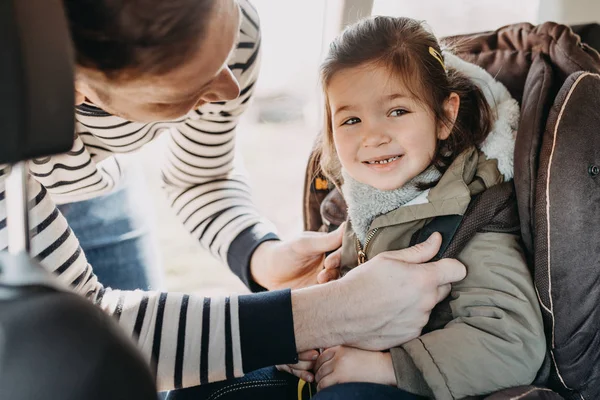 Vader dochter peuter in de vacht verbogen in haar baby-autostoeltje beveiligen — Stockfoto
