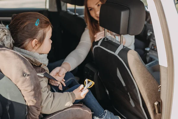 Mère sécurisant sa fille tout-petit bouclée dans son siège auto de bébé à partir du siège avant — Photo