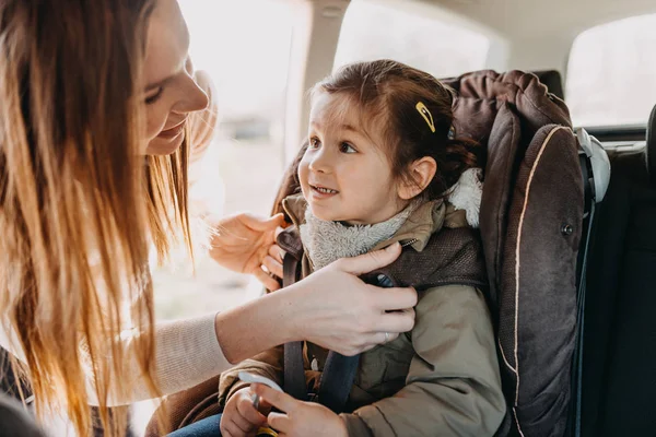 Moeder haar peuter dochter in de vacht beveiligen rammelde intoher baby autostoel — Stockfoto