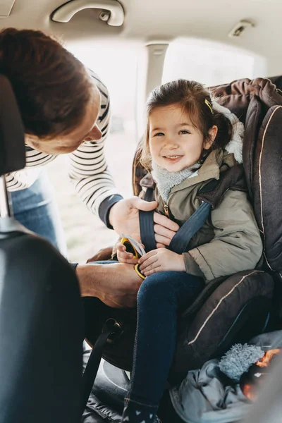 Father securing his toddler daughter in the coat buckled into her baby car seat — Stock Photo, Image