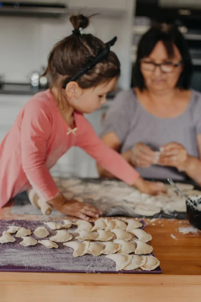 Kleinkind rollt Teig für Pirogi mit Großmutter in der Küche am Haus — Stockfoto