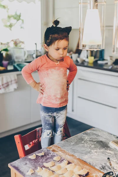 Ein kleines Mädchen steht in der Küche und trägt mit Mehl verschmutzte Kleidung — Stockfoto