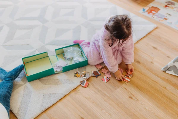 Kleines Mädchen mit braunen Haaren sammelt ein Puzzle auf dem Fußboden in th — Stockfoto