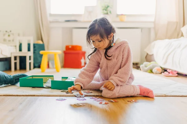 Kleines Mädchen mit braunen Haaren sammelt ein Puzzle auf dem Fußboden in th — Stockfoto