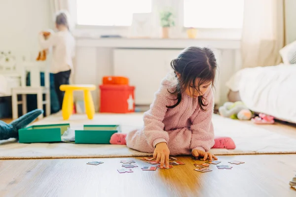 Kleines Mädchen mit braunen Haaren sammelt ein Puzzle auf dem Fußboden in th — Stockfoto