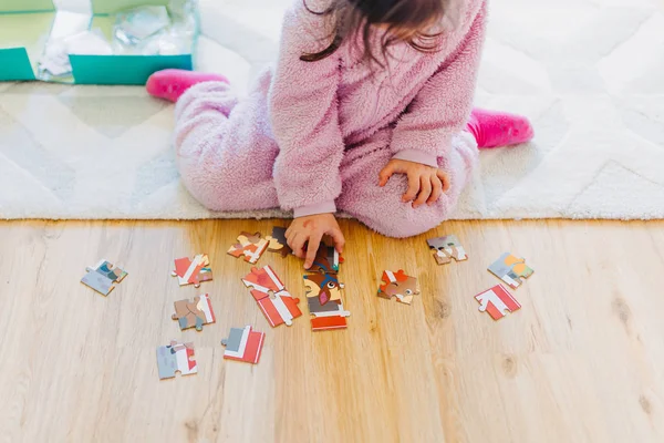 Kleines Mädchen mit braunen Haaren sammelt ein Puzzle auf dem Fußboden in th — Stockfoto