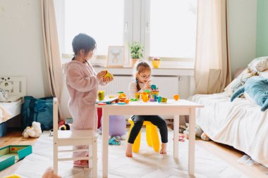 İki küçük kız çocuk odasında hamurla oynuyorlar.