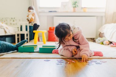 Kahverengi saçlı küçük kız yerde bir yapboz topluyor.