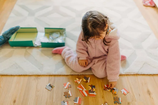 Kleines Mädchen mit braunen Haaren sammelt ein Puzzle auf dem Fußboden in th — Stockfoto