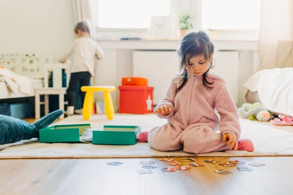 Kleines Mädchen mit braunen Haaren sammelt ein Puzzle auf dem Fußboden in th — Stockfoto