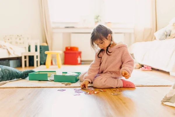 Kleines Mädchen mit braunen Haaren sammelt ein Puzzle auf dem Fußboden in th — Stockfoto