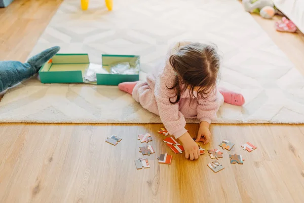 Маленькая девочка с каштановыми волосами собирает головоломку на полу в й — стоковое фото