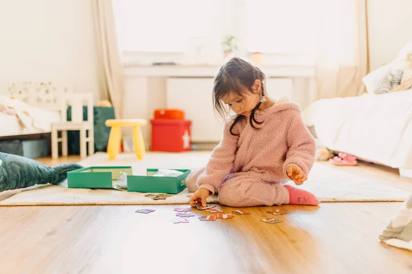 Kleines Mädchen mit braunen Haaren sammelt ein Puzzle auf dem Fußboden in th Stockbild