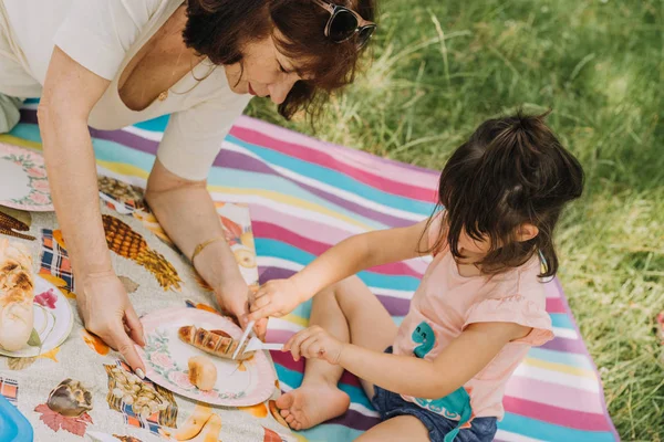 Abuela ayudando a su nieta comiendo de salchicha a la parrilla. —  Fotos de Stock