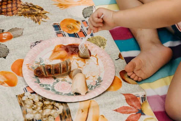 Niña comiendo salchicha a la parrilla con tenedor y cuchillo sentado un —  Fotos de Stock