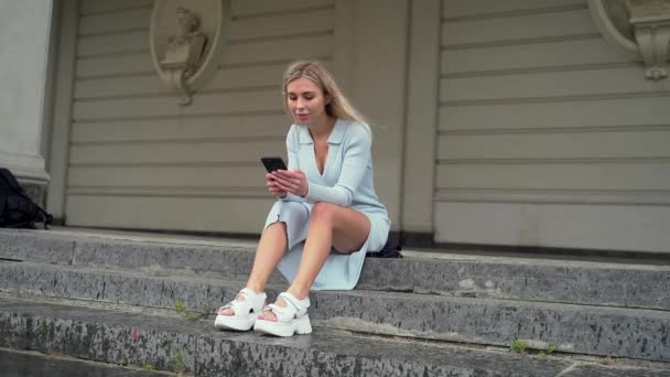 Beyaz Elbiseli Sandaletli Çekici Genç Kız Merdivenlerde Otururken Telefon Kullanıyor — Stok video