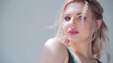 Makyajlı ve saç stili olan genç seksi sarışın kadın portresi. Spor giyim bölümündeki fitness kızı yana bakıyor ve kameraya bakıyor, yeşil gözlü. Gülümsüyor. Kapalı alanda. Stüdyo beyaz arka plan. Rüzgâr