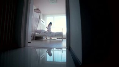 Küçük genç kız sabah yatak odasında uyanıyor, kalkıyor pencereye geliyor ve ellerini kaldırıyor. Siluet çocuk yataktan kalkıyor. Sessiz, rahat çocuk odası.
