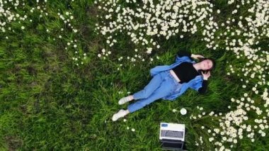 Genç hippi kız çiçeklerin arasında çimlerde dinleniyor kulaklıkla müzik dinliyor rahatlıyor. Bayan öğrenci yaşam tarzı rahatlama ve sakinlik. Parkta çimlerin üzerinde sessiz bir yer. Üst hava görüntüsü