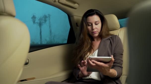 一位自信的商业女性经理坐在白色皮革豪华轿车后座上的画像 他手里拿着平板电脑或笔记本电脑工作 穿西装的女经理雨停在窗外 — 图库视频影像