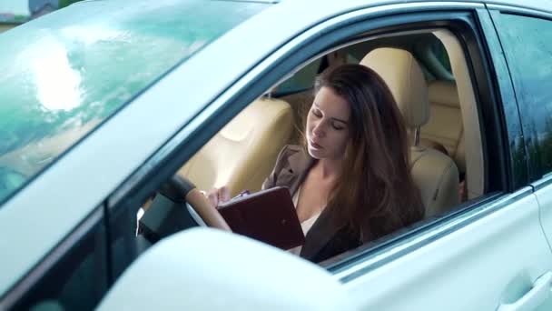 車の車輪の後ろに座っている女性マネージャーの肖像画 高級白い車の中で女性ビジネス女性 ブローカーはデータを操作して書き込みます — ストック動画