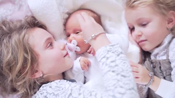 三个可爱的小孩躺在床上 姐妹俩拥抱并亲吻新生婴儿 女孩们幸福地依偎在一起的画像 快乐和微笑在一起 — 图库视频影像