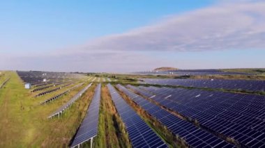 Büyük bir alan güneş panelleriyle kaplıdır. Güneş, güneş panellerinden yansıyor. Ufuk. Hava manzaralı. Yeşil tarlalarla çevrili. Güneş çiftliğinin en üst görüntüsü. modern yenilenebilir enerji
