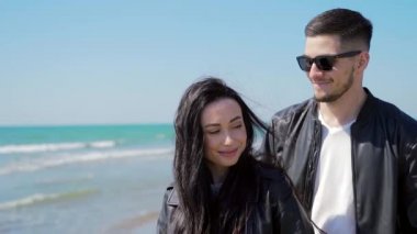Birbirine aşık genç bir çiftin yakın portresi. Kafkasyalı yüzü. Adam kıza sıkıca sarılıyor. Adam kadını arkadan öpüyor. Denizin arka planında. Kum suyu ve dalgalar. Doğa