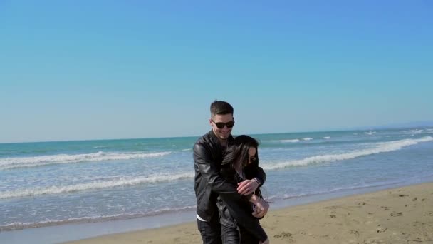 幸せな若いカップルの男と黒の服の女の子は サングラスを歩いて黒髪で海で楽しむことを受け入れる スタイリッシュなファッション女性と男性が手を携えて 海の砂の自然 — ストック動画
