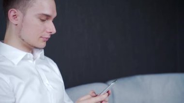  Bir adam kanepeye oturur ve telefonu tutar. Mesajlar yazar ve okur. Gülümsüyor