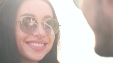 yakın plan portre, esmer kız gülümsüyor ve adama bakıyor, adam güneş gözlüklerine yansıyor. Dışarıda mutlu bir gülümseme, yaz ya da sonbahar. Şık, mutlu, çekici bir kadın..